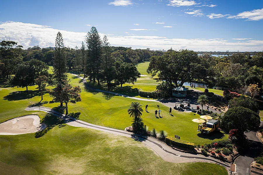 Low aerial over a fairway with players putting beside a yellow drinks cart under umbrellas