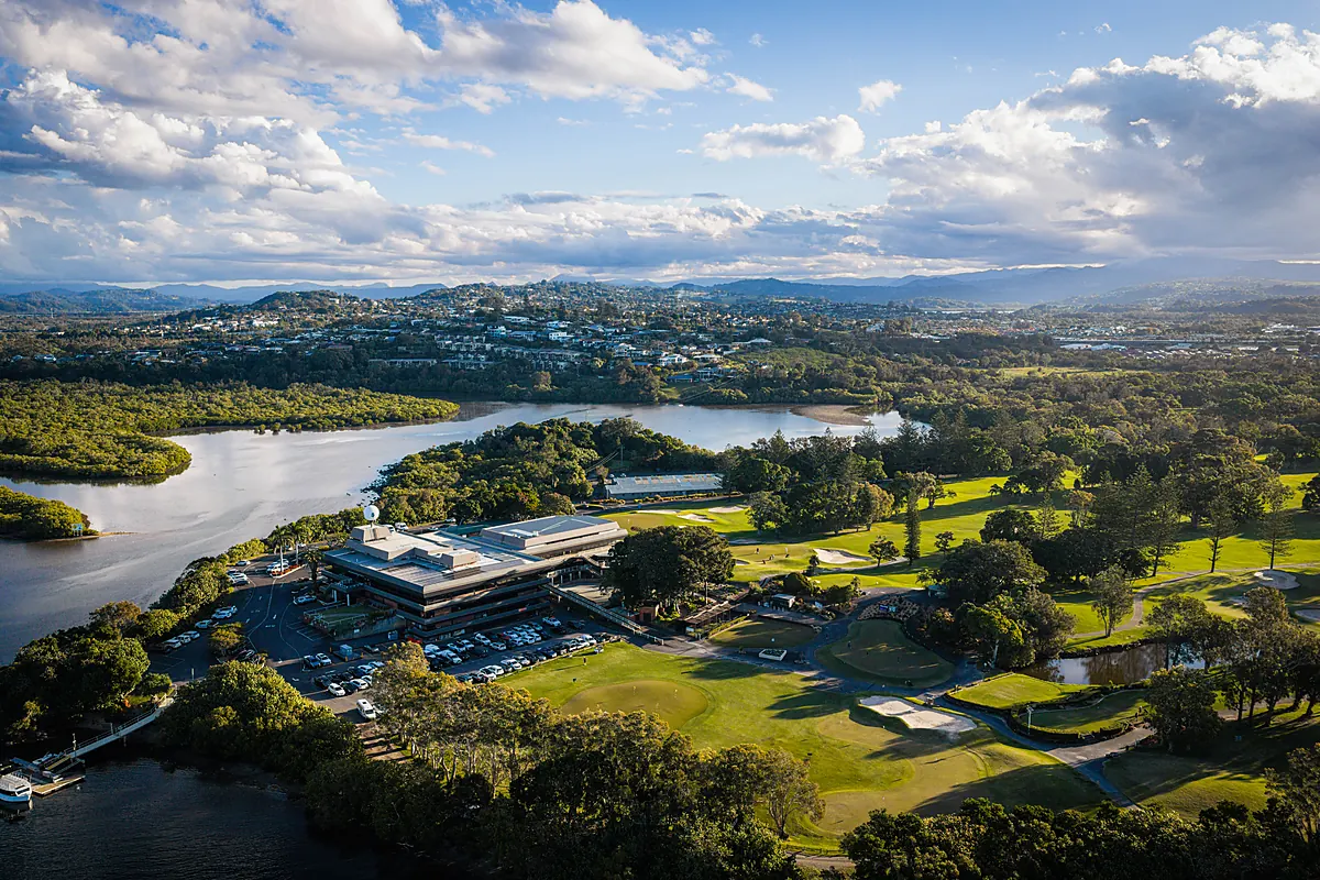 Golden-hour aerial of the clubhouse and course with the Terranora Broadwater and hinterland ranges behind