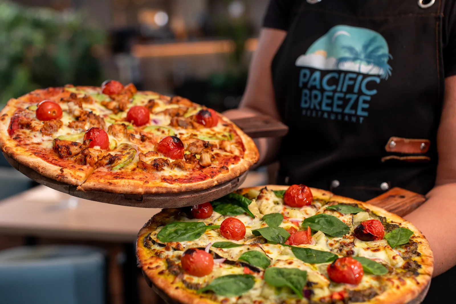 A chef presenting two woodfired pizzas at Pacific Breeze restaurant